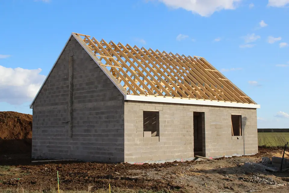Maison individuelle en construction à Ablis, murs en parpaings de béton montés et charpente en bois posée avant la couverture du toit.