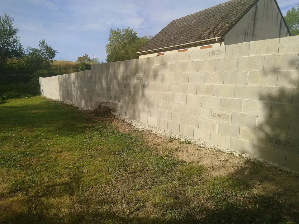 Long mur de clôture en parpaings de béton non enduits, monté en bordure d'une pelouse devant un bâtiment à Blanzy.